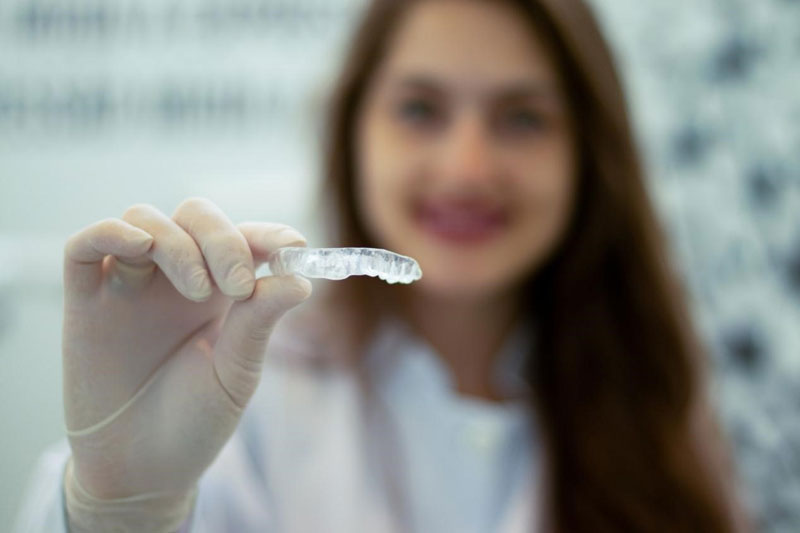 Woman wearing gloves and holding a plastic retainer.