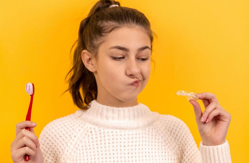 A girl holding a toothbrush that helps clean your mouthguard or retainer